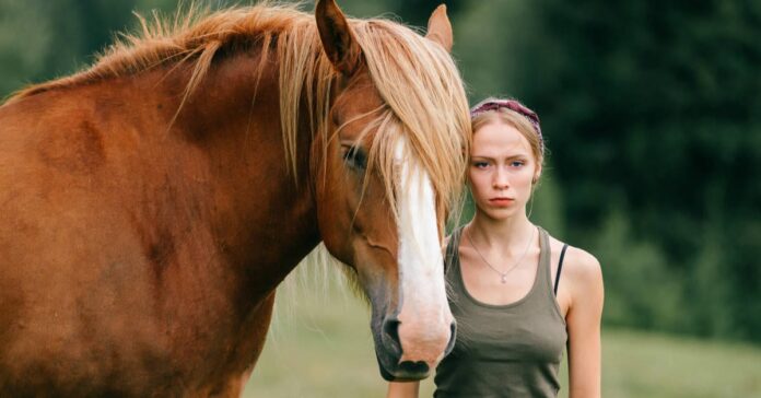 Moody horse person a young woman looking serious stands next to a chesnut horse